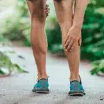 Close-up of a runner holding their calf, representing an athletic injury, muscle strain, or chronic leg pain that requires treatment.
